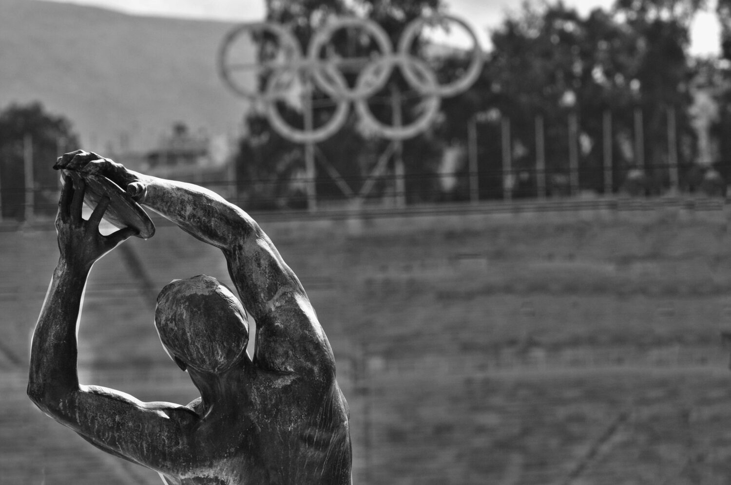 A black and white image of a statue throwing a discus with the Olympic rings in the background